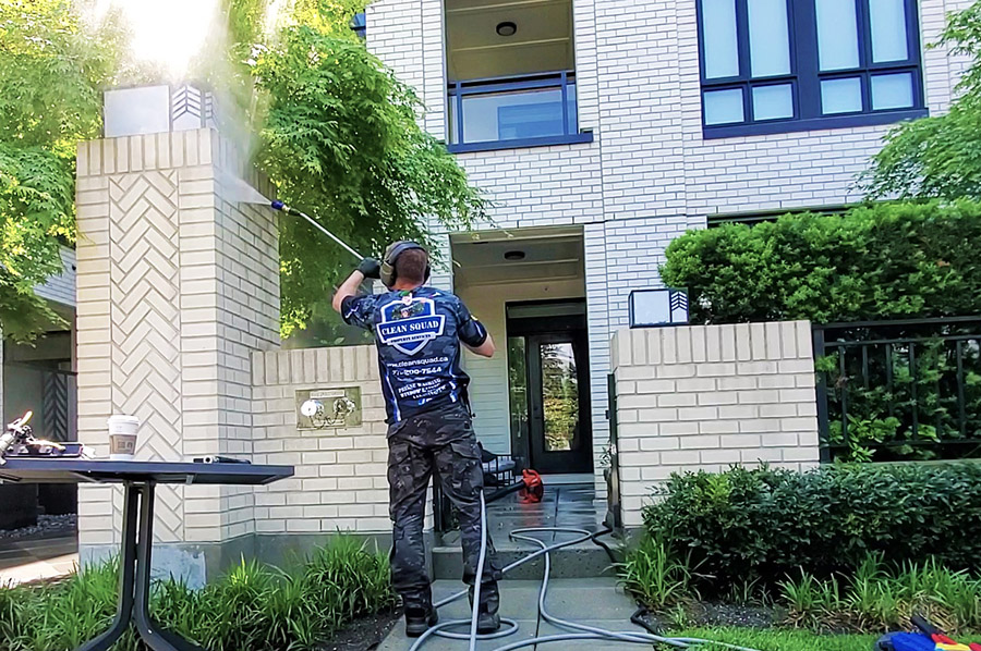 a clean squad employee pressure washing brick building siding